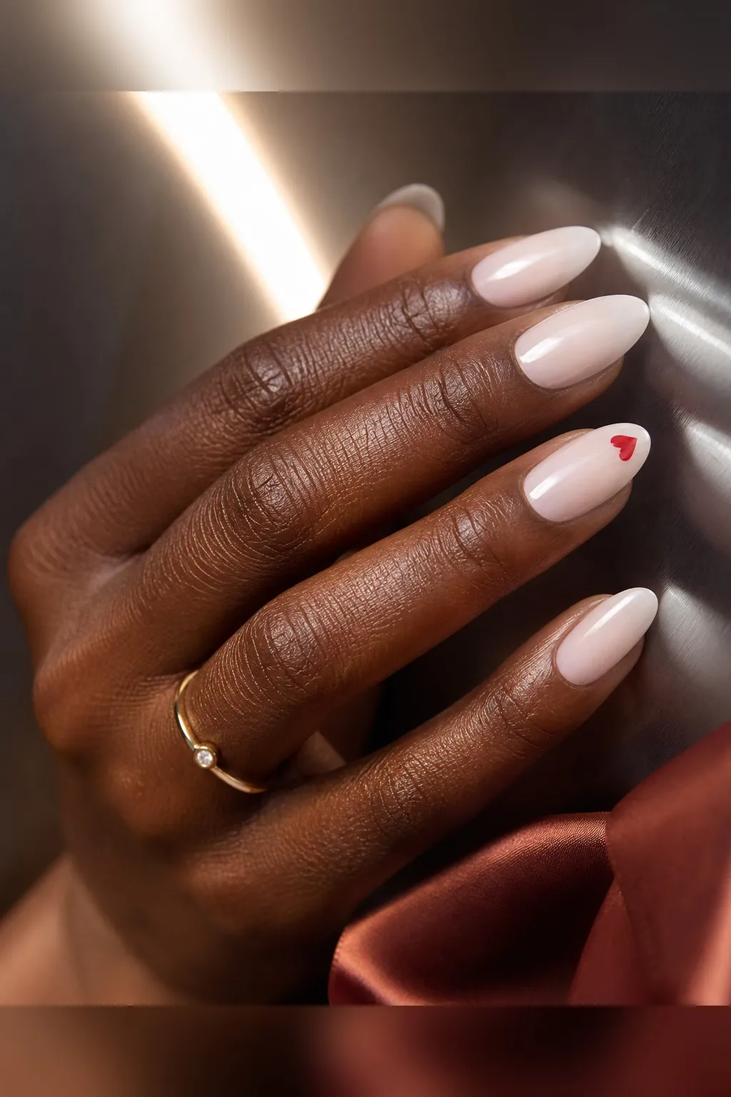 Red Heart Accent — almond red nails with sheer milky base on every nail, with one small red heart near the tip of each ring finger, glossy…