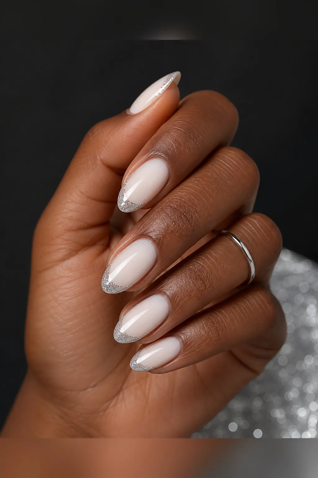 Silver Glitter French — almond winter nails with sheer milky base with fine silver glitter french tips along a clean smile line, glossy seal…
